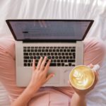 Eine Frau sitzt mit ihrem Laptop und einem Kaffee auf dem Bett. In meinem Text verdient sie Geld mit Dropshipping.